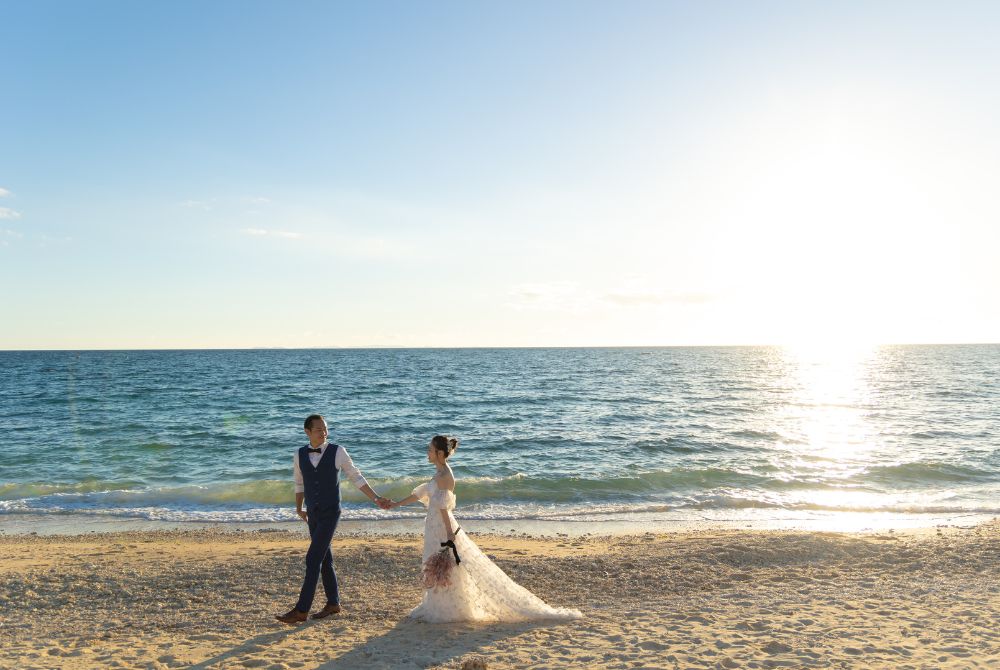 青いタキシードの新郎とホワイトドレスの新婦がビーチを散策