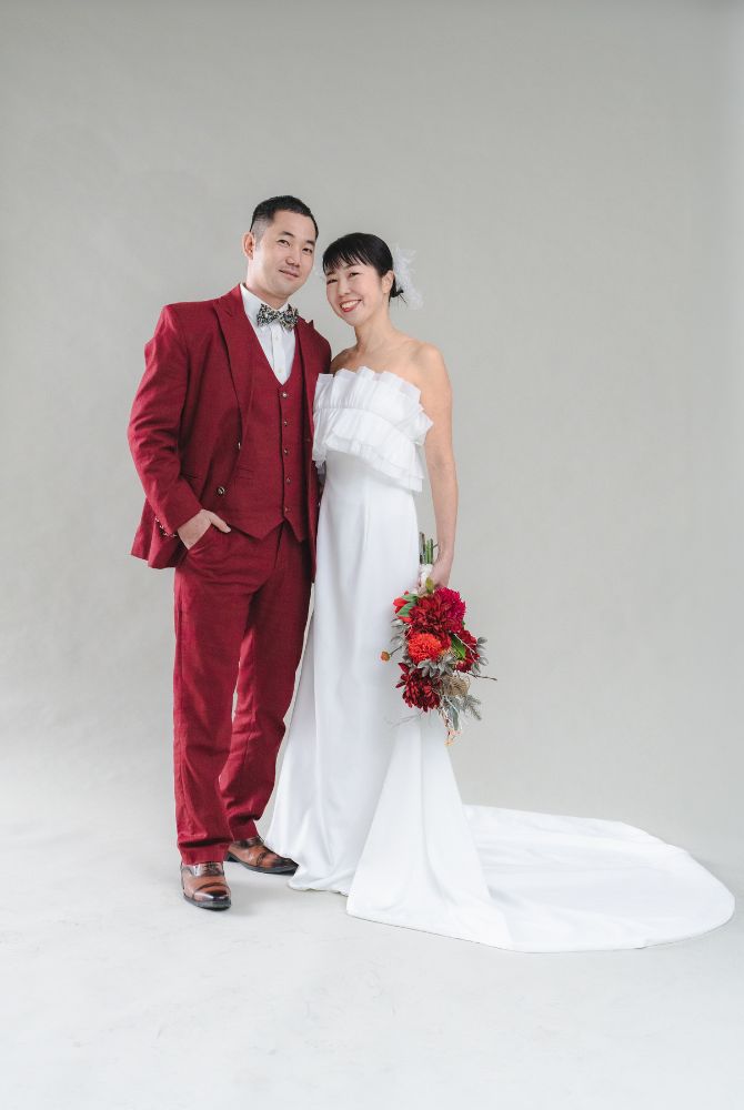 バーガンディのタキシードの新郎とホワイトドレスの新婦のスタジオショット